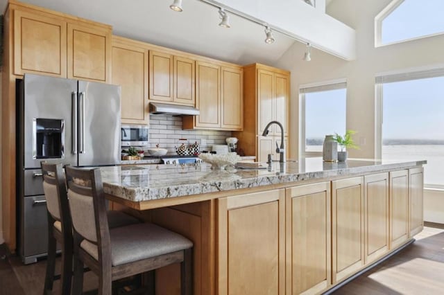 kitchen featuring appliances with stainless steel finishes, tasteful backsplash, light brown cabinetry, a water view, and light stone counters