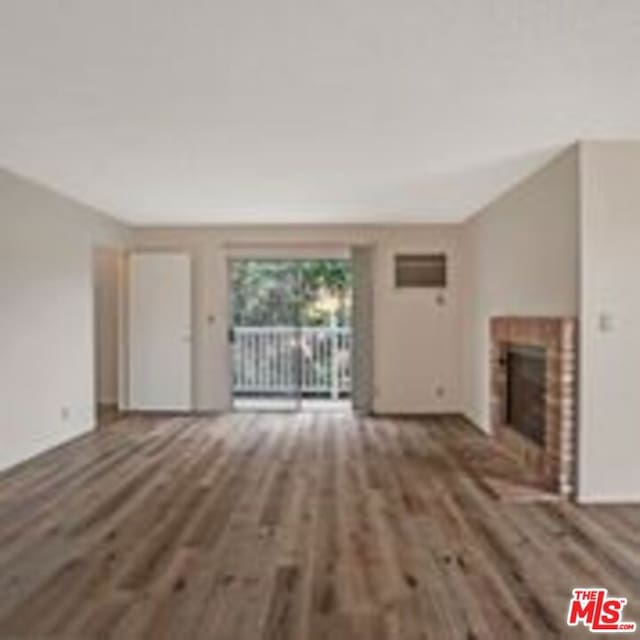 unfurnished living room featuring a brick fireplace and dark hardwood / wood-style floors