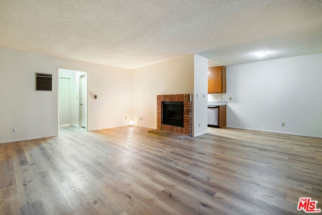 unfurnished living room featuring a brick fireplace, light hardwood / wood-style floors, and a textured ceiling