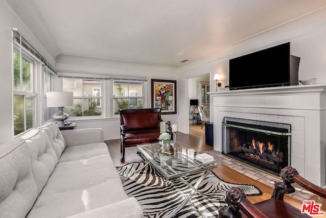 living room featuring a healthy amount of sunlight, wood-type flooring, and a brick fireplace