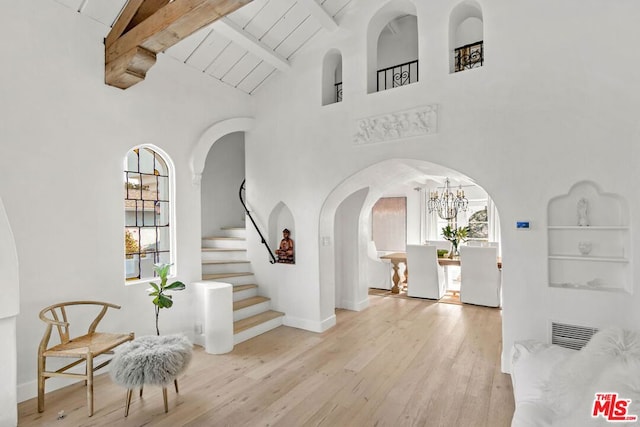 foyer entrance with high vaulted ceiling, beam ceiling, a notable chandelier, and light wood-type flooring