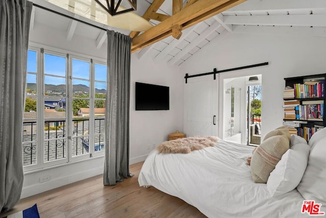 bedroom with light hardwood / wood-style floors, multiple windows, a barn door, and vaulted ceiling with beams