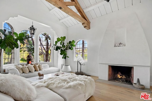 living room featuring high vaulted ceiling, a large fireplace, light hardwood / wood-style flooring, and beam ceiling