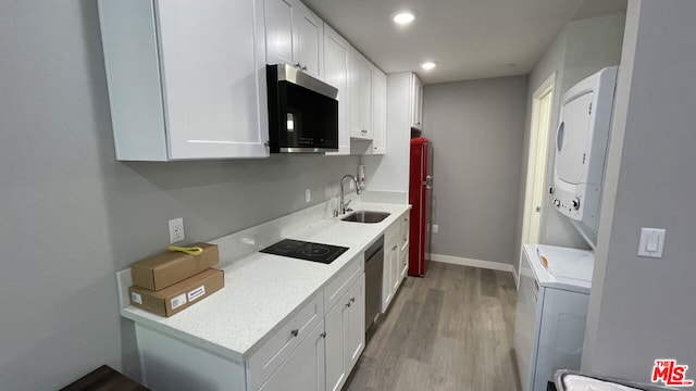 kitchen featuring stainless steel appliances, light wood-type flooring, stacked washer / dryer, white cabinets, and sink