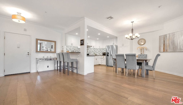 dining space with ornamental molding, light hardwood / wood-style flooring, and an inviting chandelier