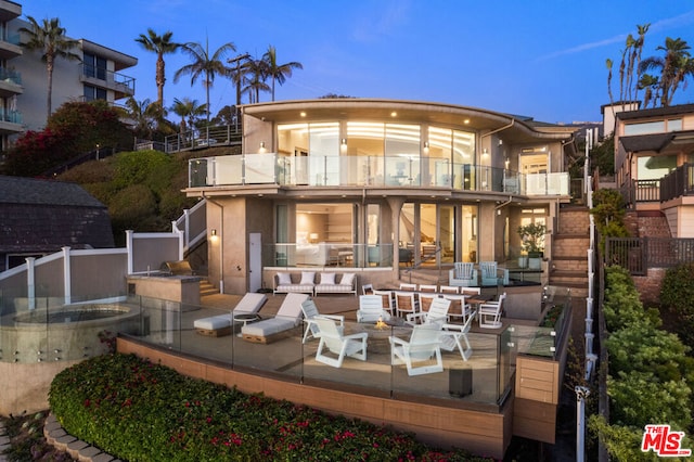 back house at dusk featuring an outdoor living space with a fire pit, a patio area, and a balcony