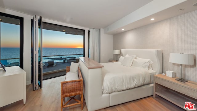 bedroom with light hardwood / wood-style floors, access to outside, a water view, and floor to ceiling windows