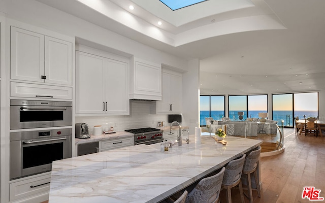 kitchen featuring a breakfast bar, white cabinetry, light stone countertops, appliances with stainless steel finishes, and dark hardwood / wood-style flooring