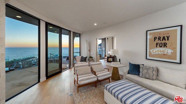 living room featuring light wood-type flooring, a water view, and expansive windows