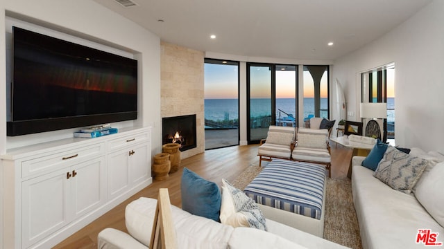 living room featuring light hardwood / wood-style floors, a large fireplace, a wall of windows, and a water view