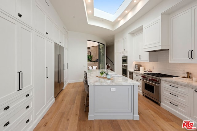 kitchen featuring a skylight, an island with sink, high quality appliances, white cabinets, and sink