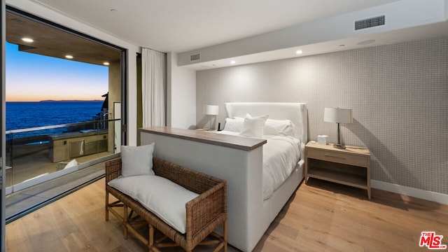 bedroom with light hardwood / wood-style floors and a water view