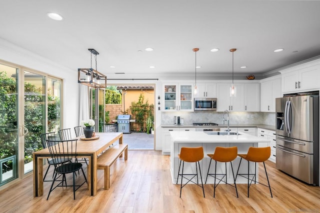 kitchen featuring white cabinetry, a center island with sink, stainless steel appliances, decorative backsplash, and pendant lighting