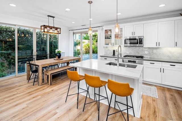 kitchen featuring light hardwood / wood-style floors, backsplash, a kitchen island with sink, decorative light fixtures, and white cabinets