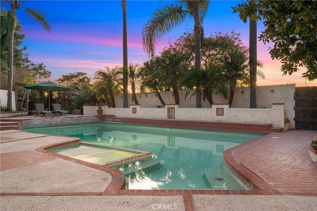 pool at dusk featuring a patio and a jacuzzi