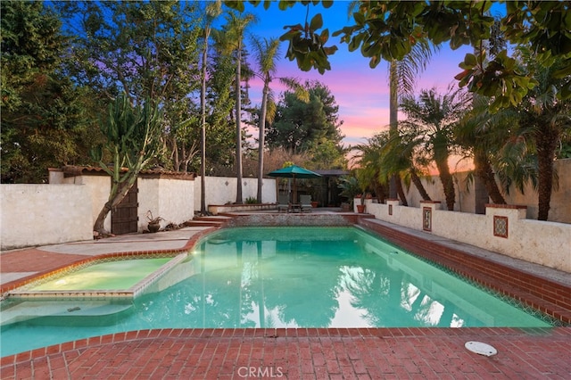 pool at dusk featuring an in ground hot tub