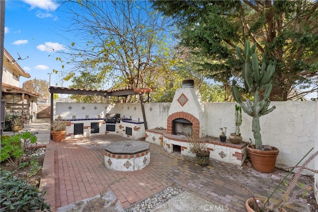 view of patio featuring exterior kitchen, an outdoor brick fireplace, and a fire pit