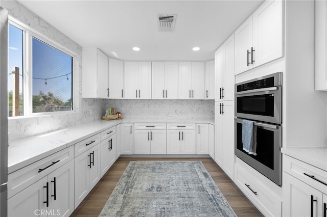 kitchen with tasteful backsplash, light stone countertops, white cabinets, and double oven