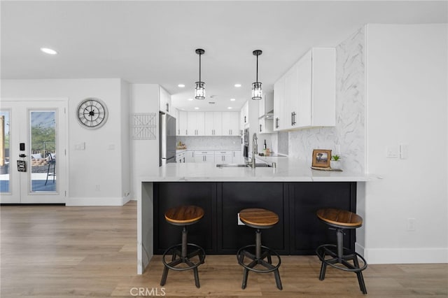 kitchen with a breakfast bar area, tasteful backsplash, stainless steel refrigerator, kitchen peninsula, and white cabinets