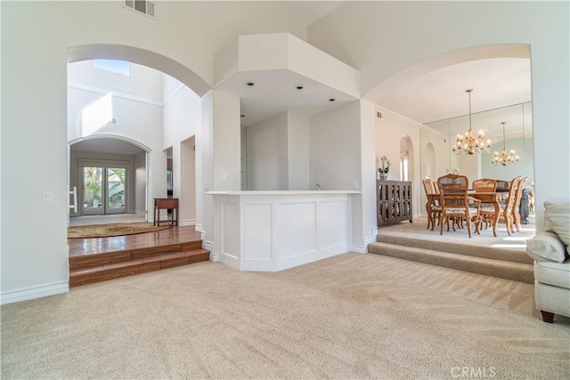 unfurnished living room with an inviting chandelier, high vaulted ceiling, and carpet flooring