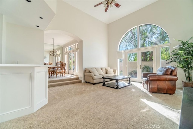 carpeted living room with ceiling fan with notable chandelier, high vaulted ceiling, and french doors