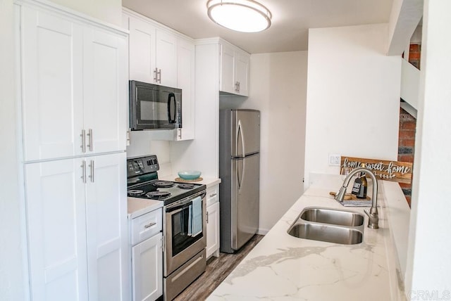 kitchen with light stone countertops, hardwood / wood-style floors, white cabinets, stainless steel appliances, and sink