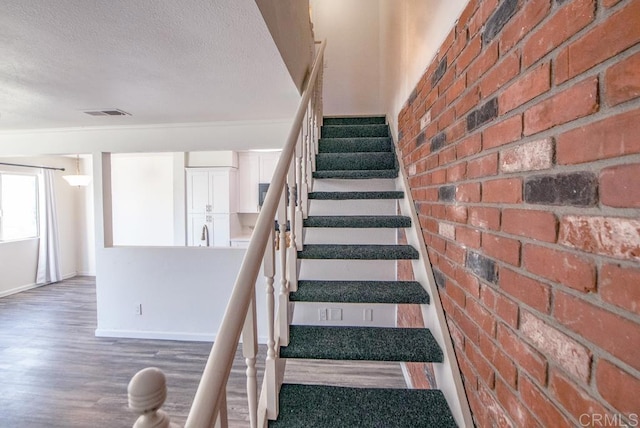 staircase with a textured ceiling, brick wall, and hardwood / wood-style flooring