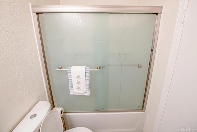 bathroom featuring toilet and shower / bath combination with glass door