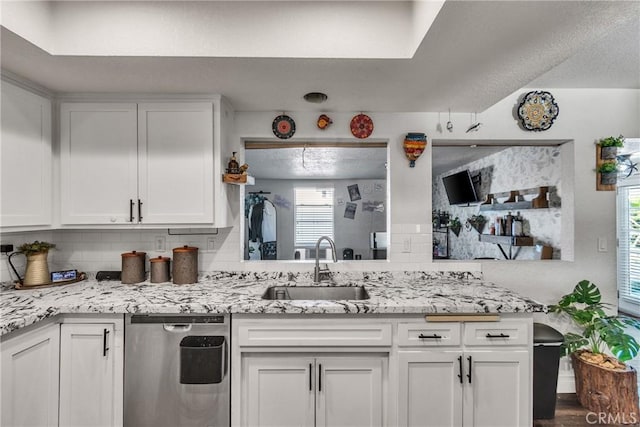 kitchen with white cabinetry, sink, light stone counters, stainless steel dishwasher, and decorative backsplash