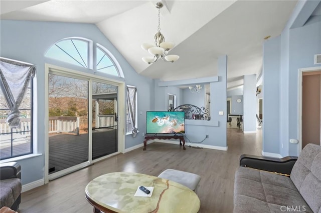 living room with a healthy amount of sunlight, vaulted ceiling, a chandelier, and hardwood / wood-style floors