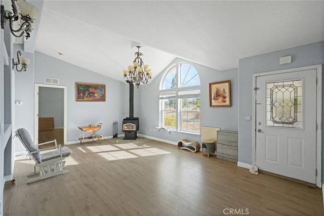 entrance foyer with lofted ceiling, a wood stove, hardwood / wood-style floors, and a notable chandelier