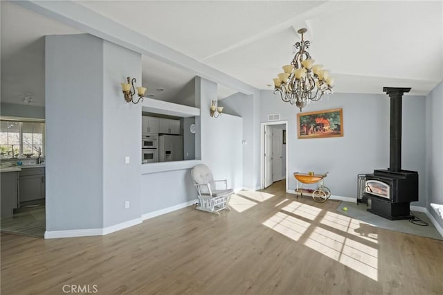 living room featuring lofted ceiling, a notable chandelier, a wood stove, and light hardwood / wood-style flooring