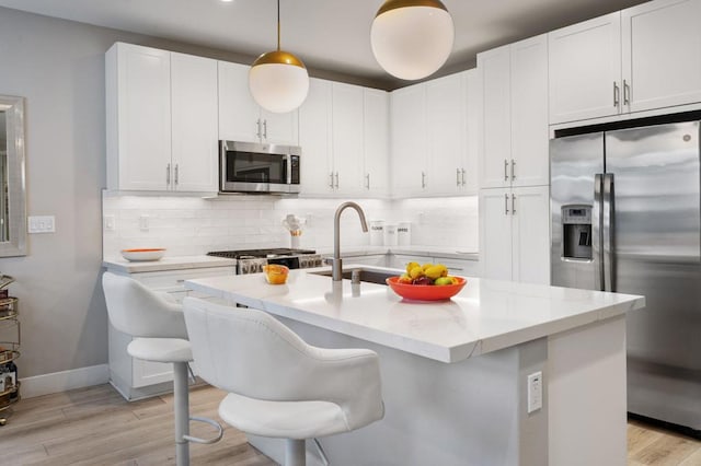 kitchen featuring decorative light fixtures, white cabinetry, appliances with stainless steel finishes, an island with sink, and a kitchen breakfast bar