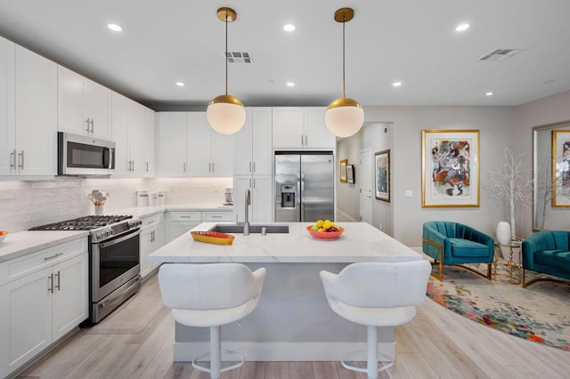 kitchen with white cabinetry, stainless steel appliances, decorative light fixtures, a kitchen breakfast bar, and sink