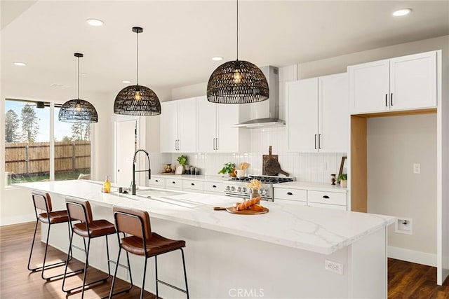 kitchen with light stone countertops, a kitchen island with sink, wall chimney exhaust hood, and pendant lighting