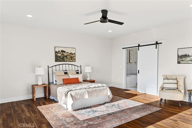 bedroom with ceiling fan, a barn door, dark hardwood / wood-style flooring, and connected bathroom