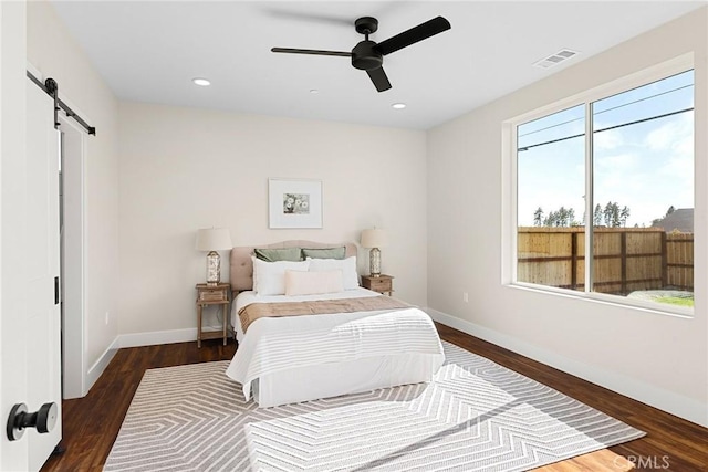 bedroom featuring ceiling fan, a barn door, and dark hardwood / wood-style floors