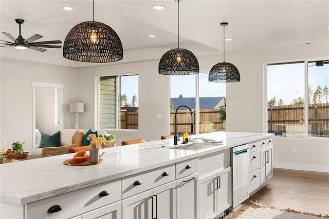 kitchen featuring dishwasher, sink, a kitchen island with sink, plenty of natural light, and white cabinets