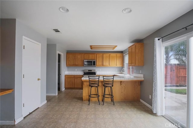 kitchen with appliances with stainless steel finishes, tile counters, sink, kitchen peninsula, and a breakfast bar area