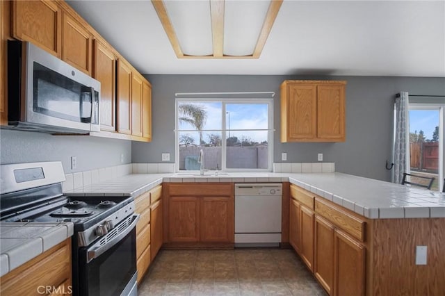 kitchen with appliances with stainless steel finishes, tile countertops, kitchen peninsula, and sink