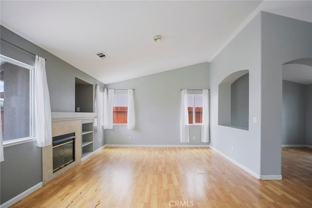 unfurnished living room featuring vaulted ceiling, a wealth of natural light, and a tiled fireplace