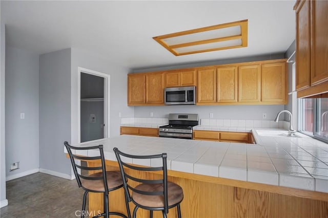 kitchen featuring tile countertops, kitchen peninsula, sink, a breakfast bar area, and stainless steel appliances