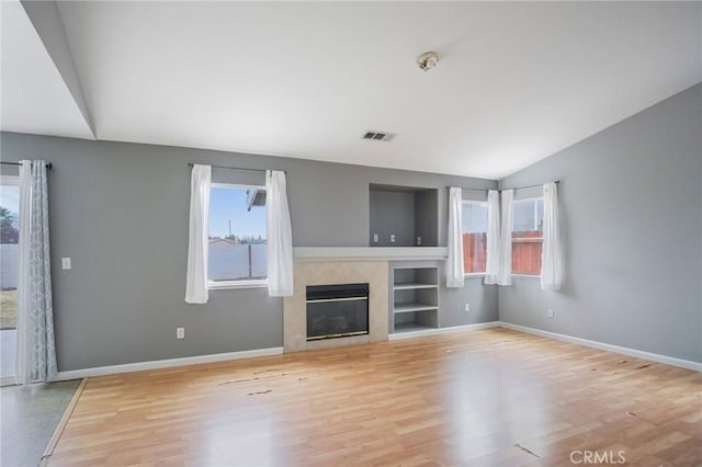 unfurnished living room with light wood-type flooring, built in shelves, and vaulted ceiling