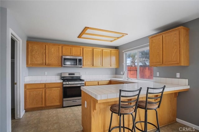 kitchen with tile counters, stainless steel appliances, sink, kitchen peninsula, and a breakfast bar area