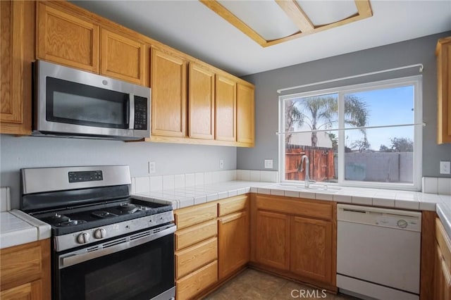 kitchen with sink, dark tile patterned floors, stainless steel appliances, and tile countertops