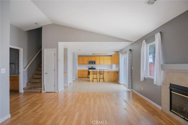 kitchen with stainless steel appliances, light wood-type flooring, a kitchen breakfast bar, a tile fireplace, and sink