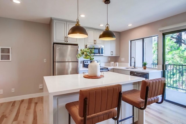 kitchen featuring pendant lighting, a kitchen bar, sink, light wood-type flooring, and appliances with stainless steel finishes