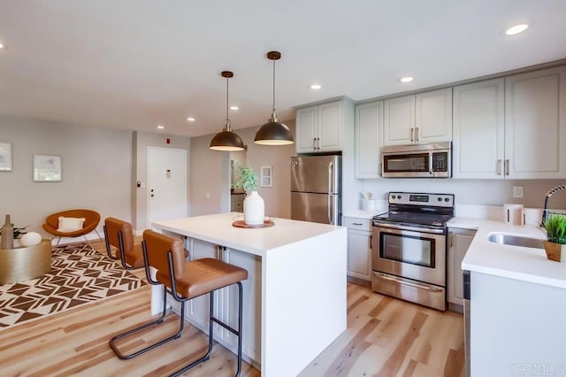 kitchen with pendant lighting, appliances with stainless steel finishes, a center island, sink, and light hardwood / wood-style flooring