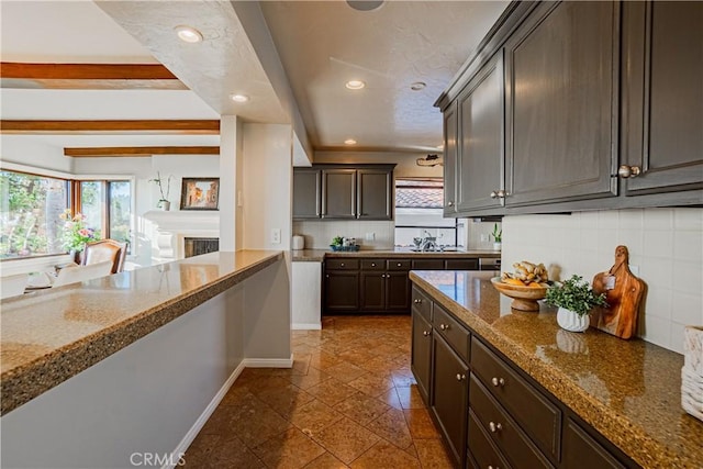 kitchen featuring light stone countertops, dark brown cabinets, beamed ceiling, and tasteful backsplash