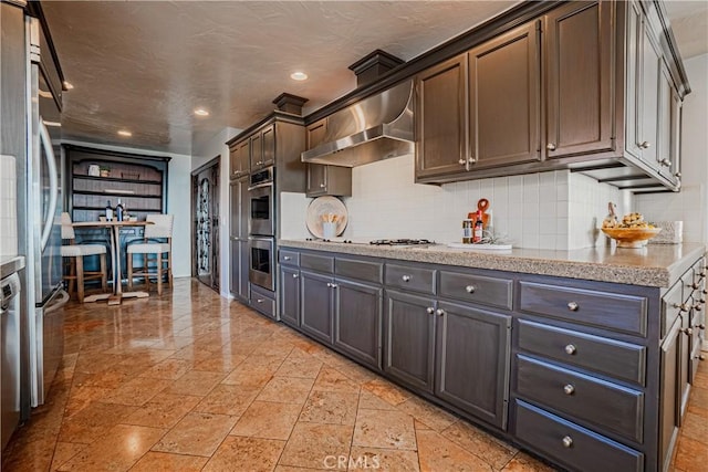 kitchen featuring decorative backsplash, stainless steel appliances, wall chimney exhaust hood, and dark brown cabinets